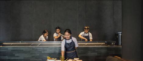 A restaurant interior with a counter, four staff members, and a table with dishes.