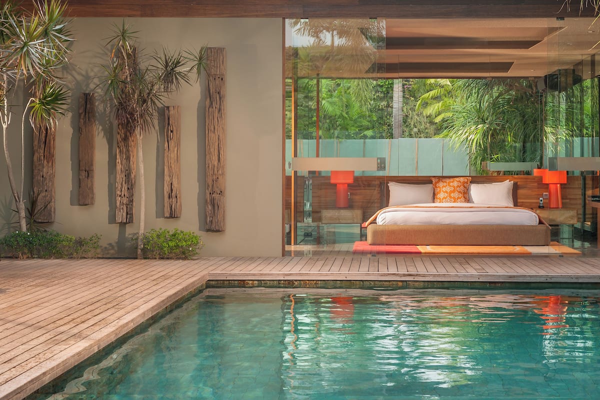 A modern bedroom with a glass wall, a wooden deck, and a pool.