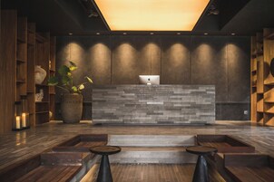 Uma área de recepção com design moderno, destacando um balcão com textura de pedra, estantes de madeira e um vaso de planta.