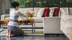 Eine Person führt ein Ritual mit Blumen auf einem Holztisch in einem Raum mit einer Couch und Kissen durch.