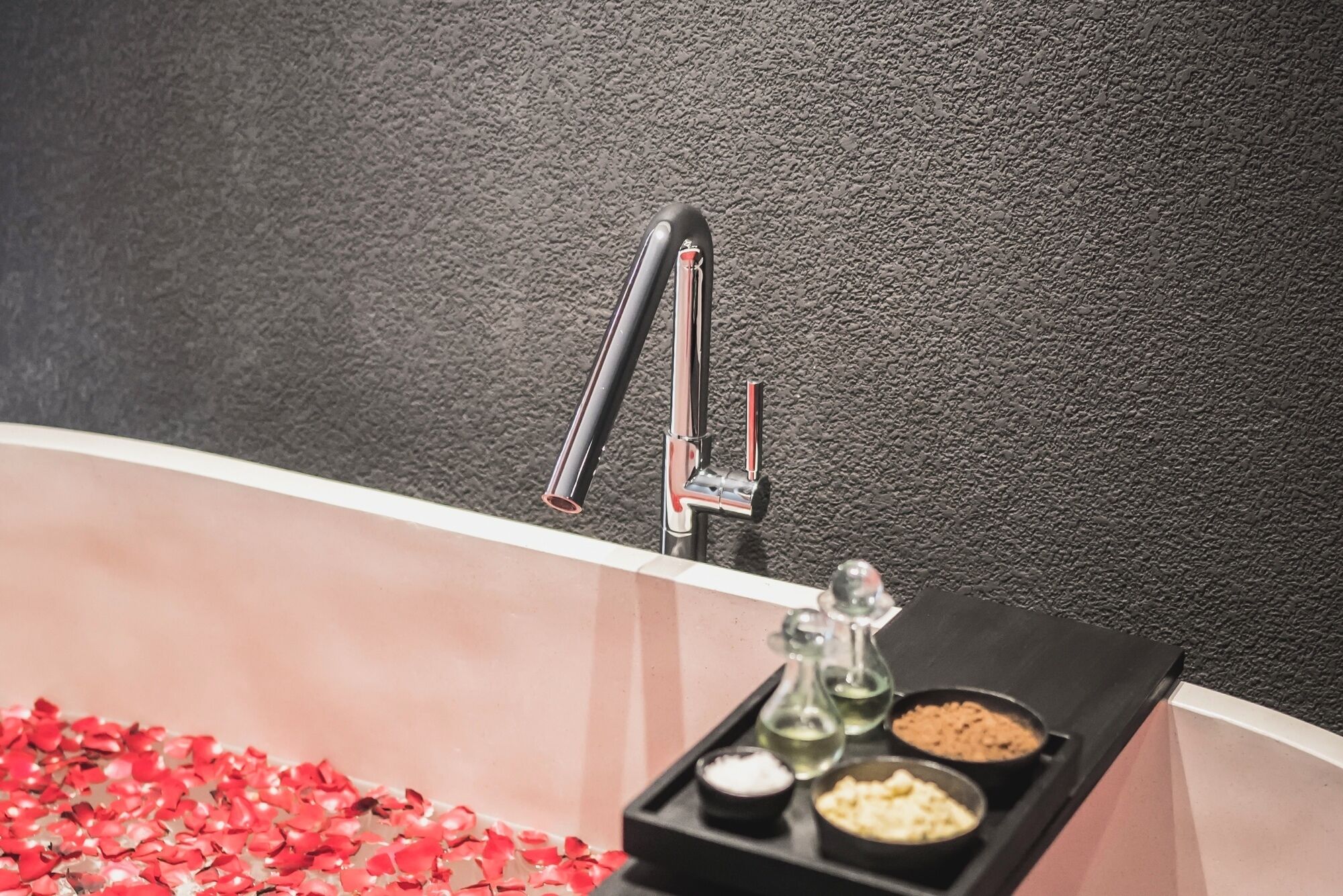 A bathroom with a black textured wall, a chrome faucet, and a tray with various toiletries.