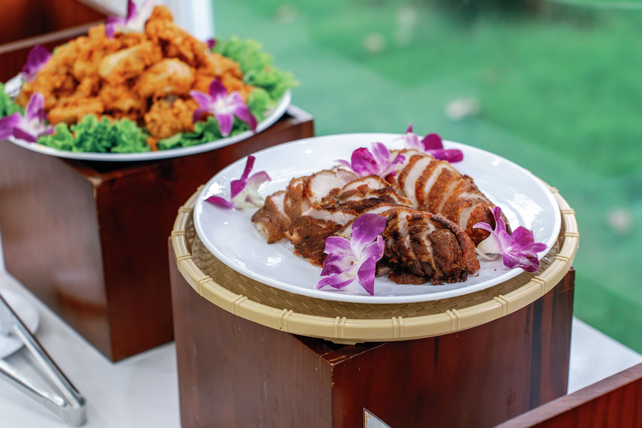 A dining table with a plate of sliced meat and a plate of fried food, both garnished with purple flowers.