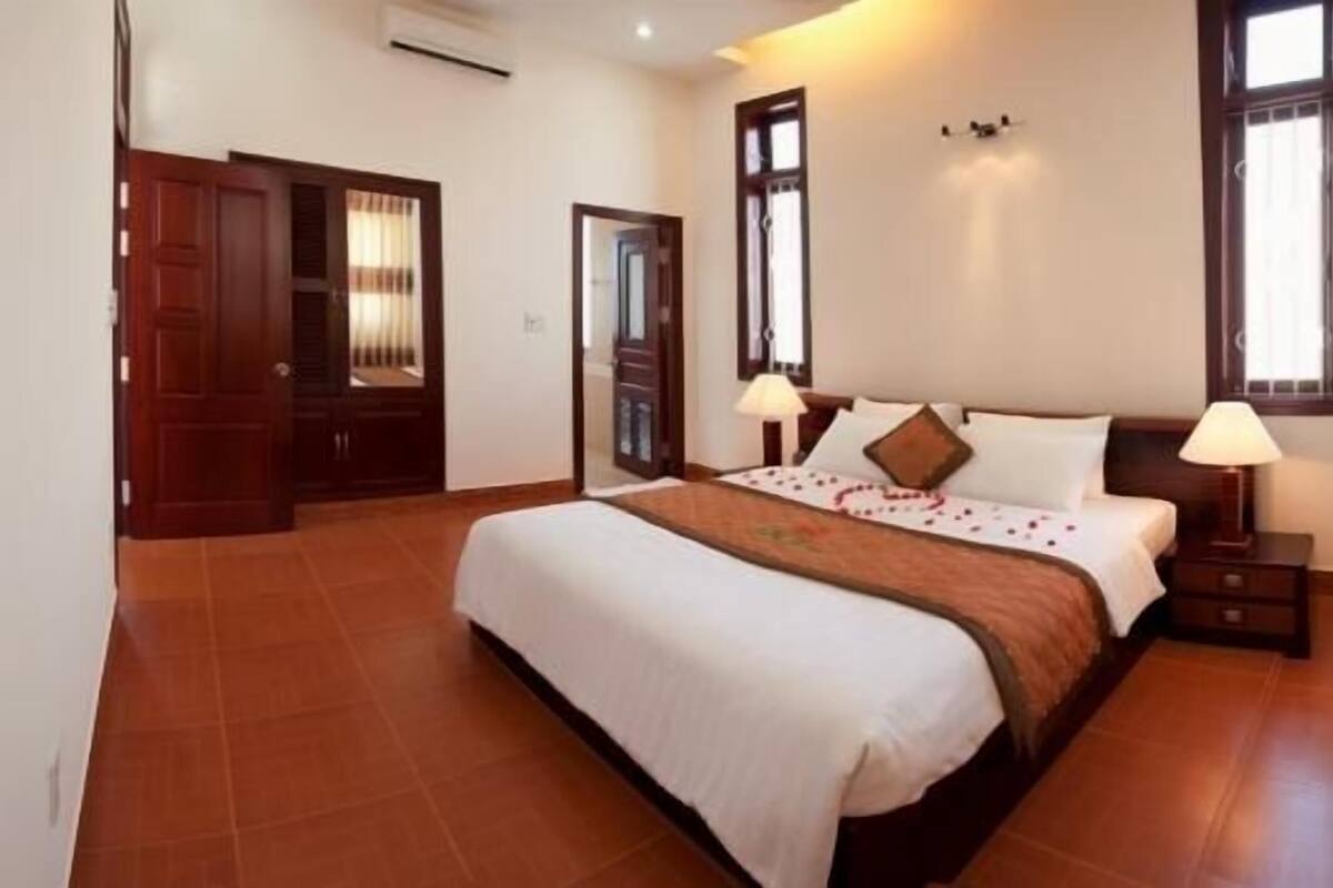 Une chambre à coucher avec un grand lit, deux tables de chevet, une commode, une fenêtre et une porte.