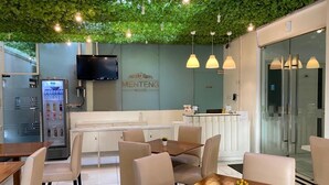 A modern dining area with a green ceiling, a kitchen area, and a reception desk. - Menteng House (Jakarta)