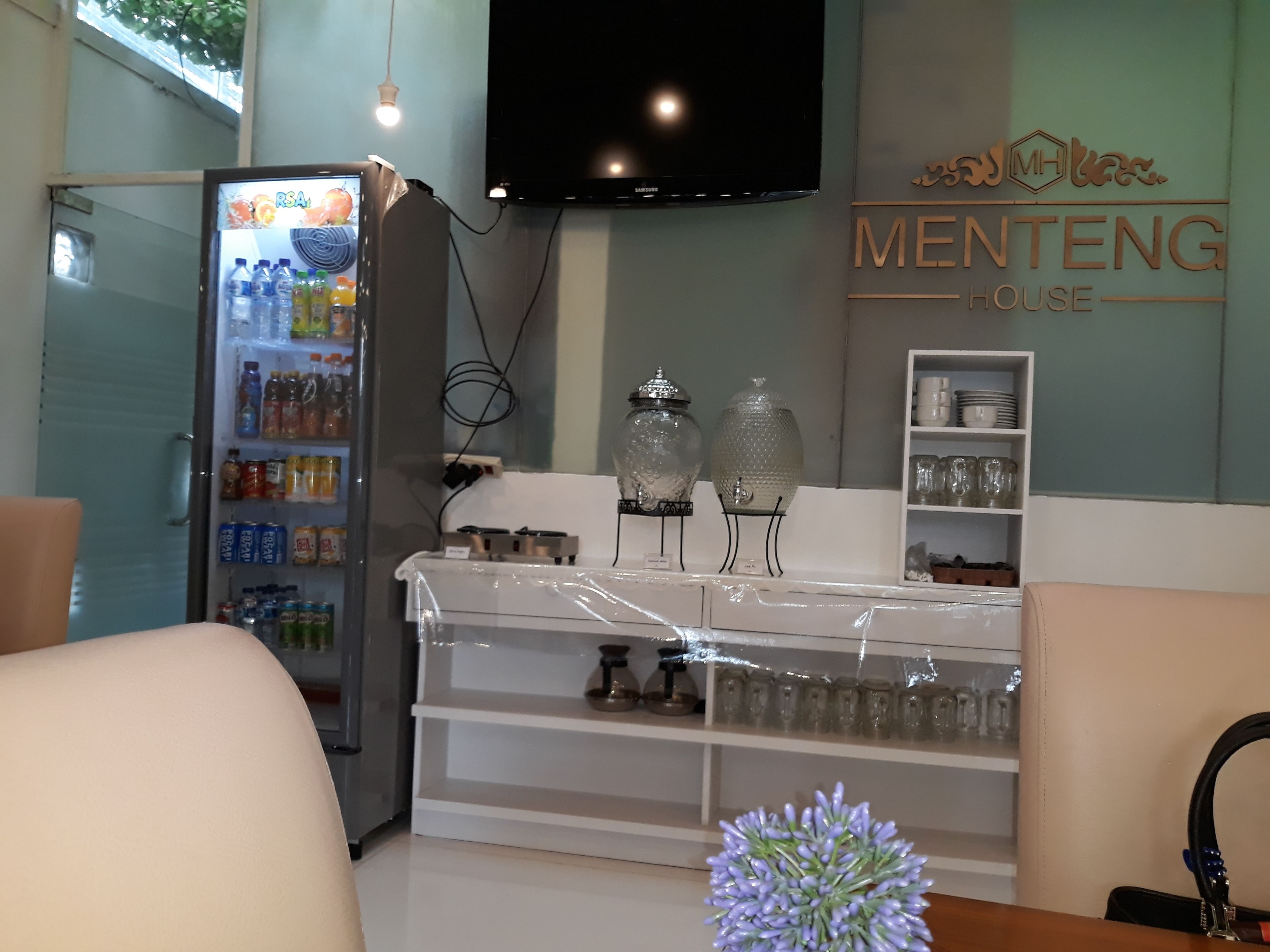 A room with a refrigerator stocked with beverages, a TV mounted on the wall, and a counter with glassware.