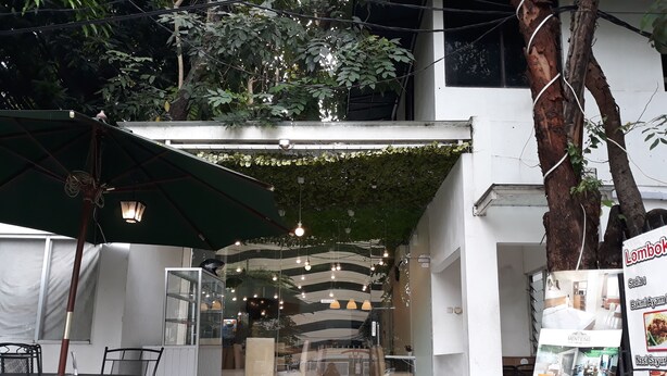 An outdoor seating area with tables and chairs, a green umbrella, and hanging lights. - Menteng House (Jakarta)