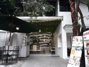 An outdoor seating area with tables and chairs, a green umbrella, and hanging lights. - Menteng House (Jakarta)