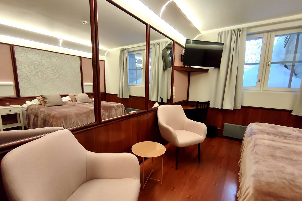 A hotel room with a large mirror, two beds, a TV, a small table, and a chair.