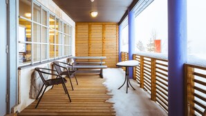 A covered outdoor area with wooden benches and chairs, a table, and a view of the snowy landscape.