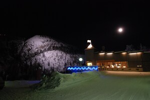 A snow-covered landscape with a building featuring a flag on top and illuminated blue lights.