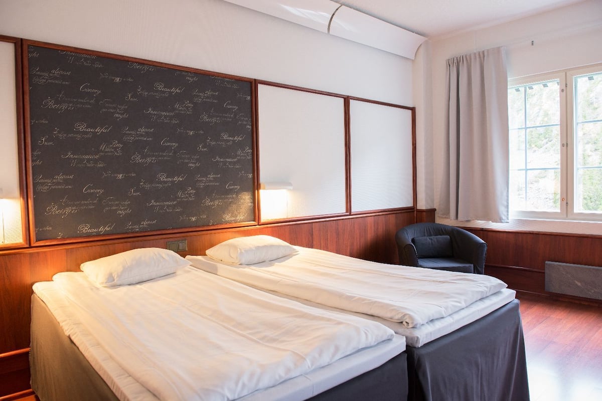 A hotel room with two beds, a large chalkboard wall, a window with curtains, and a chair.