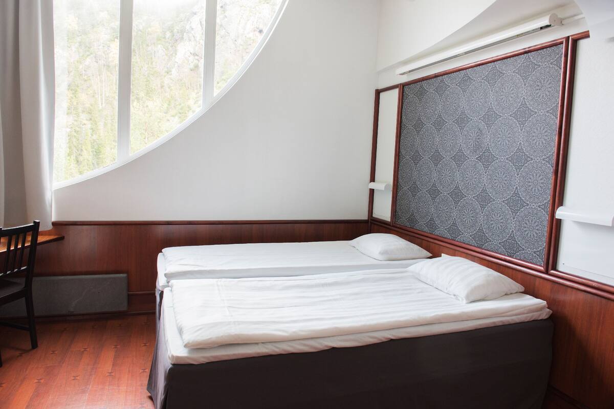 A bedroom with two beds, a window, a chair, and a patterned wall.