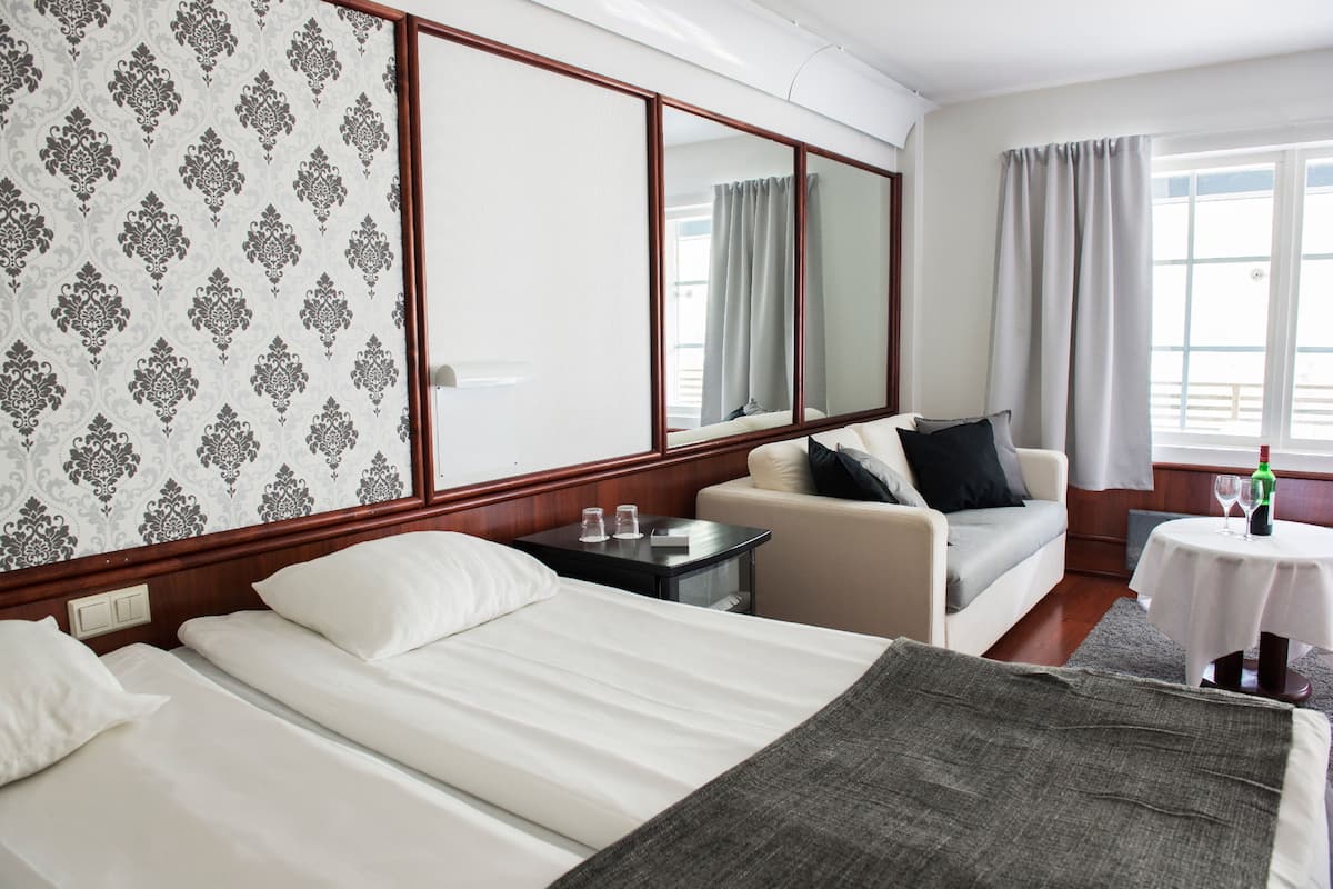A hotel room with two beds, a sofa, a small table with a glass, and a window with curtains.
