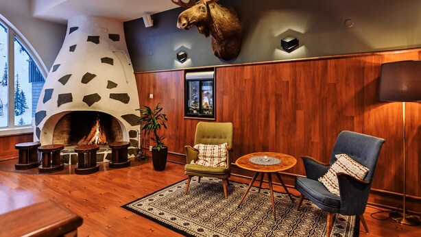 A cozy lounge area with a stone fireplace, wooden flooring, and a mounted moose head.