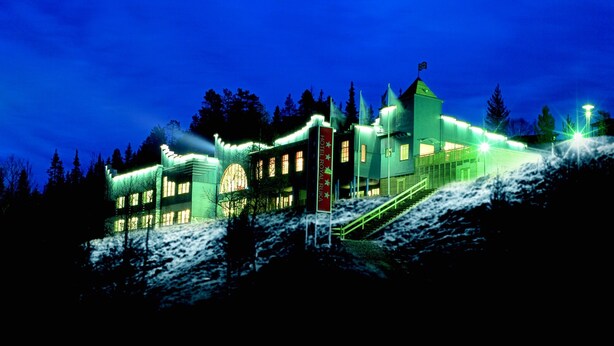 Um hotel com um edifício central imponente e alas menores, rodeado por árvores e neve.