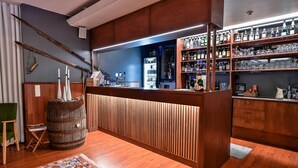 Uma área de bar com prateleiras de madeira cheias de garrafas e copos, um balcão de madeira e um tapete estampado no chão.