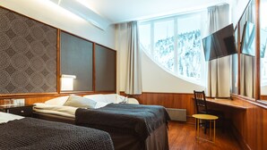 Quarto de hotel com duas camas, uma escrivaninha, uma cadeira, televisão e janela com cortinas.