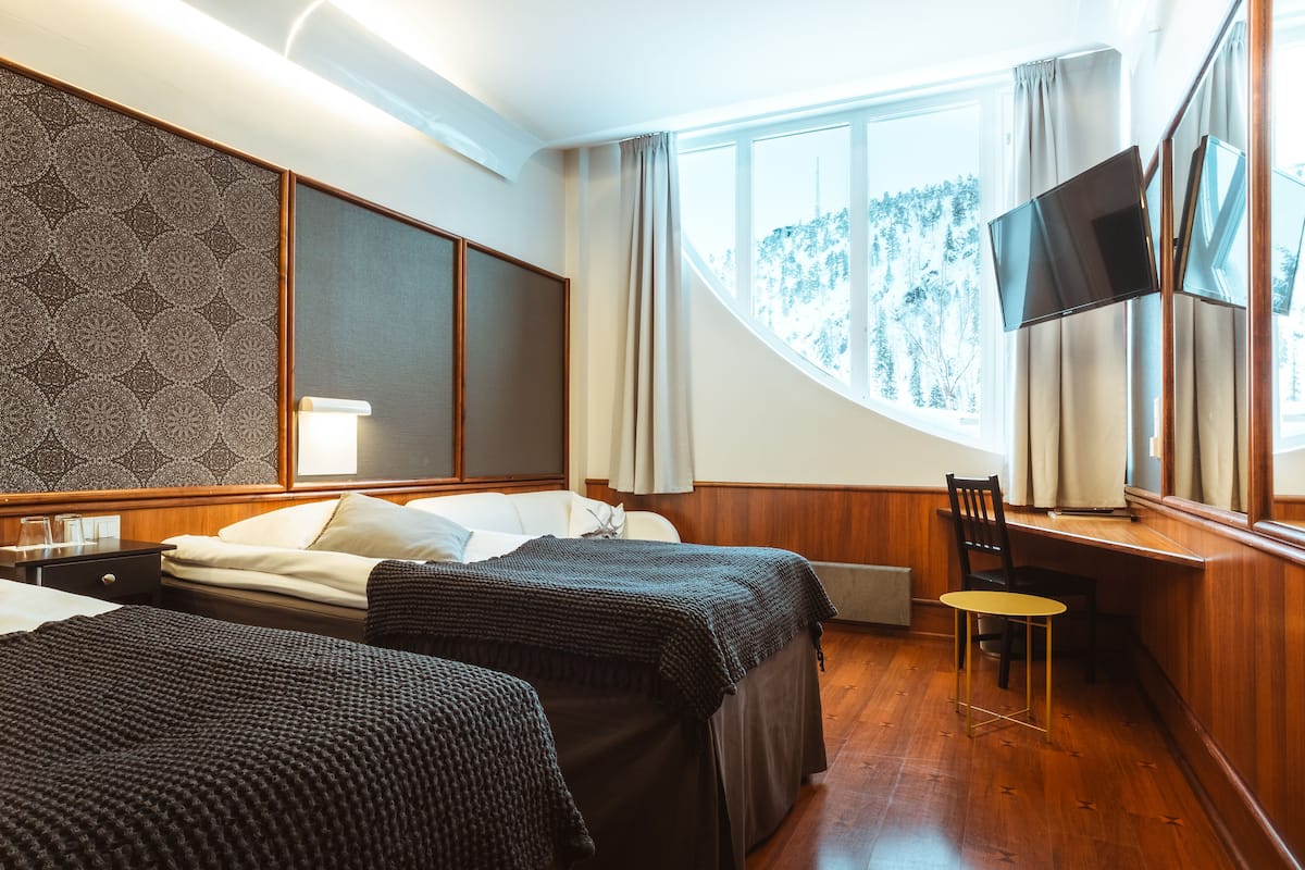 A hotel room with two beds, a desk, a chair, a TV, and a window with curtains.