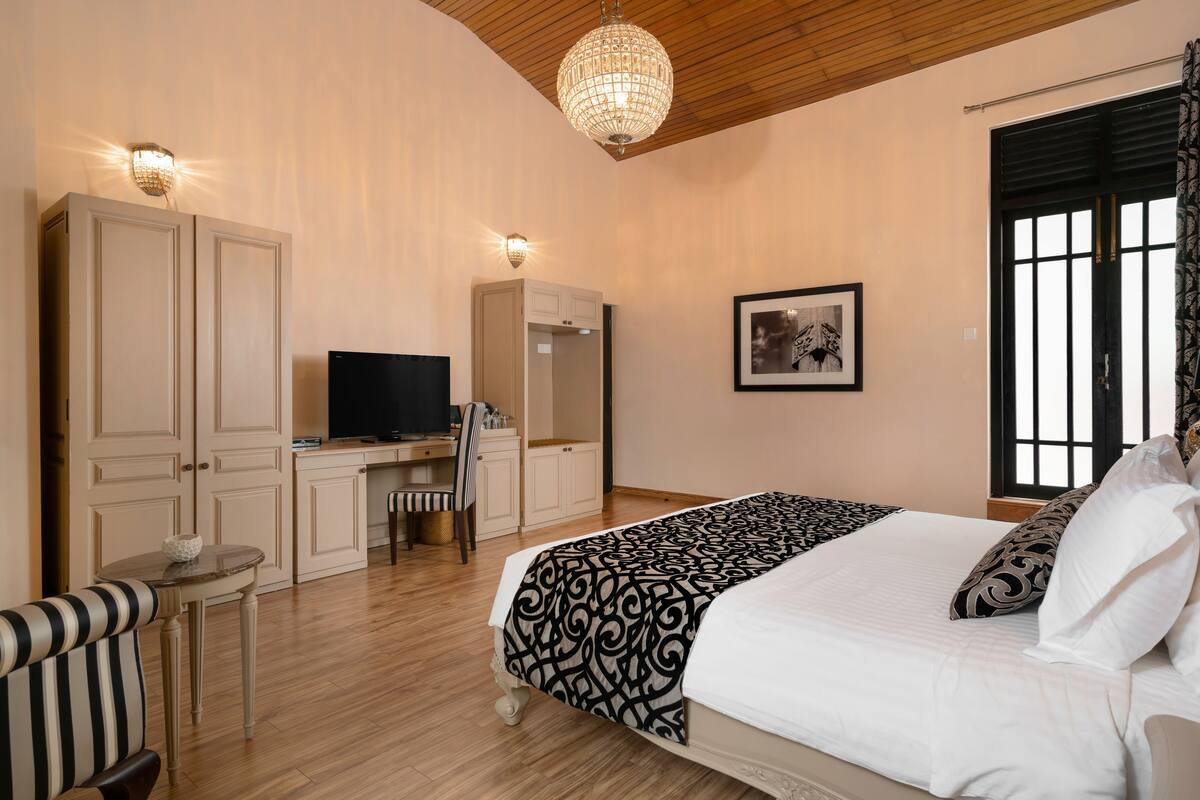 A bedroom with a large bed, a desk, a television, and a wardrobe.