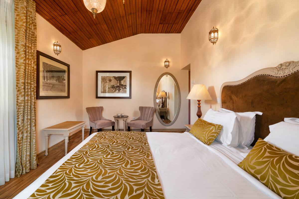 A hotel room with a large bed, two armchairs, a small table, and a mirror.