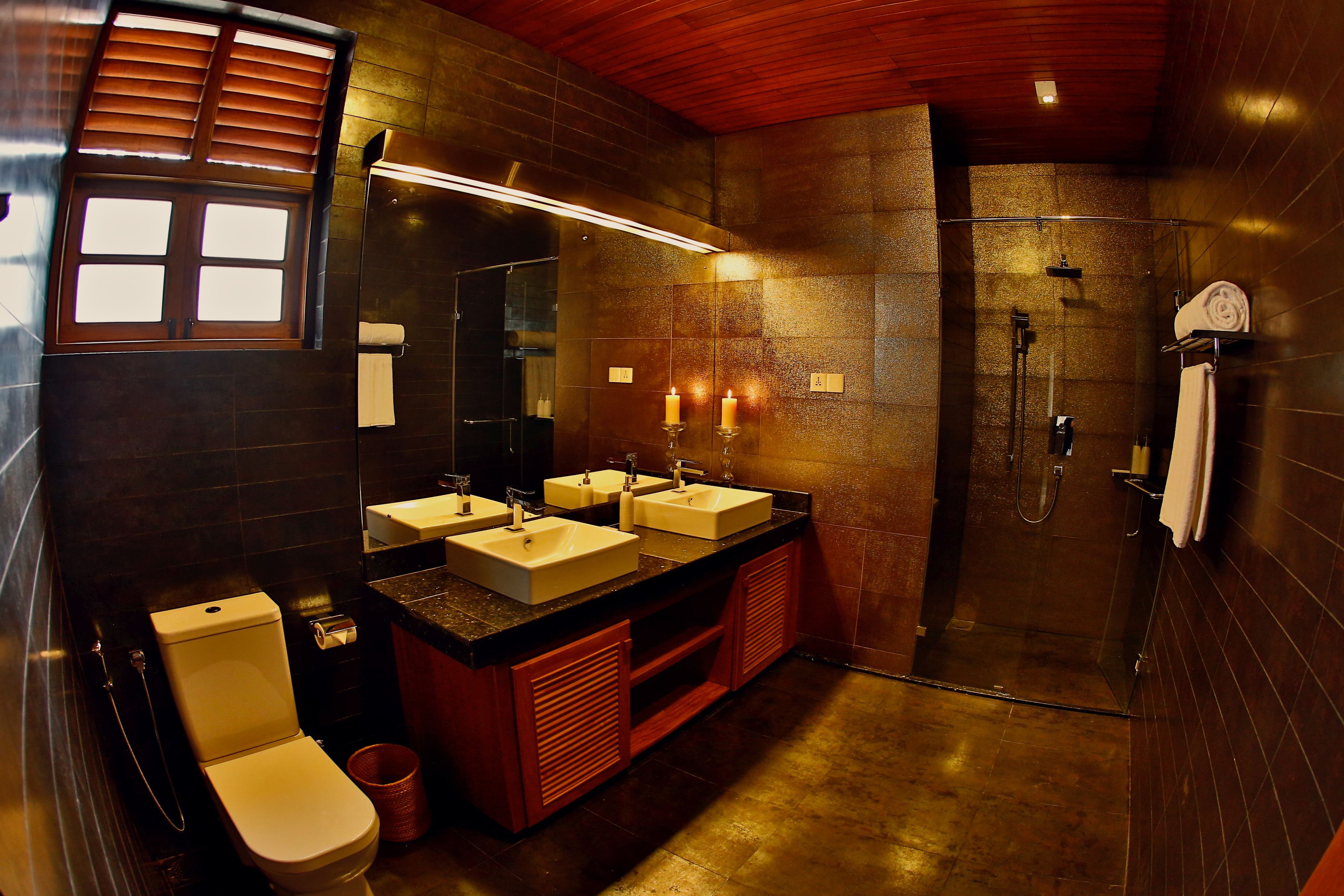 A modern bathroom with a large mirror, two sinks, a toilet, and a shower area.