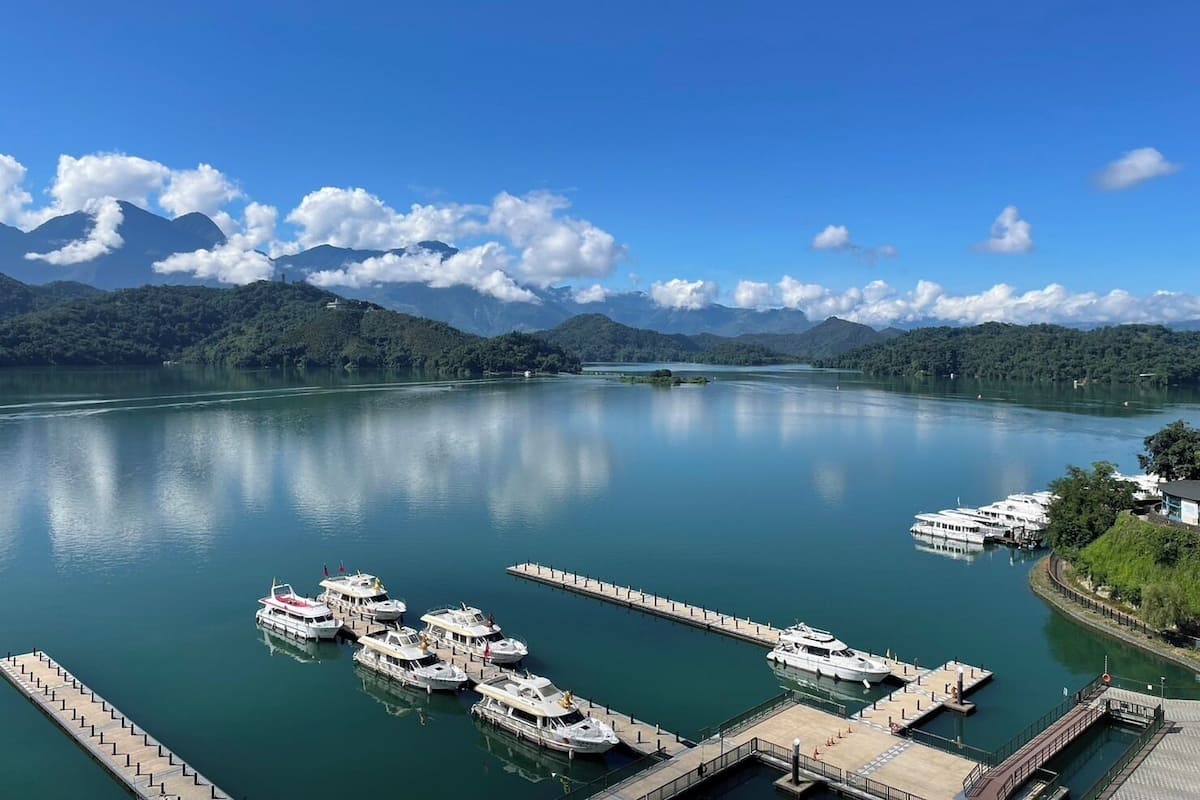 A marina with several boats docked, surrounded by mountains and clear skies.