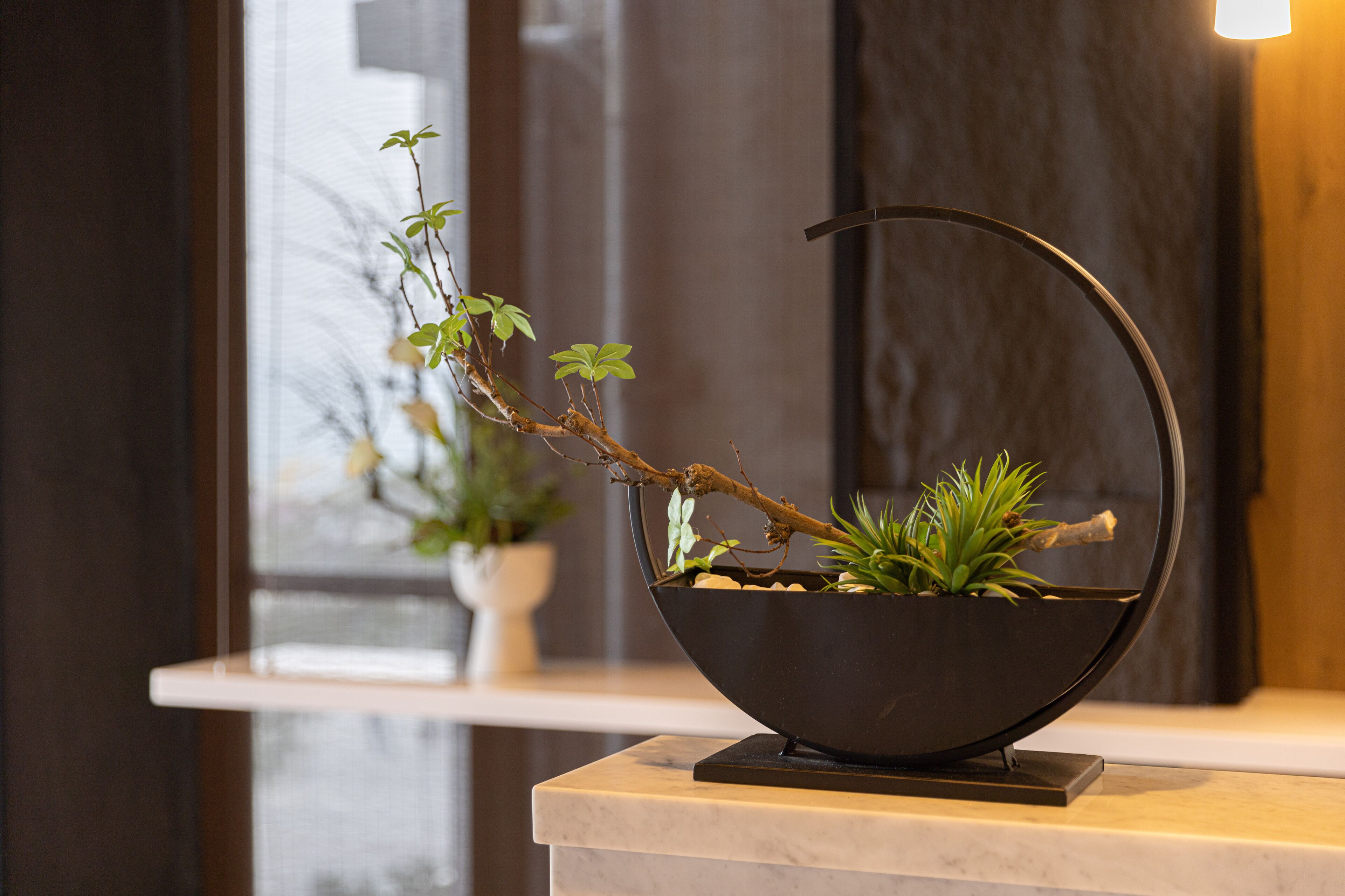 Un pot de fleurs noir, en forme de bol, doté d’une anse incurvée et posé sur un piédestal en marbre.