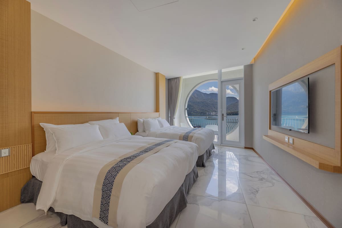 A hotel room with two beds, a large window with a view of mountains, and a flat-screen TV mounted on the wall.