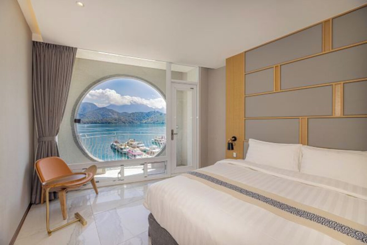 Une chambre d’hôtel avec un grand lit, une vue sur un lac et un balcon avec une chaise.
