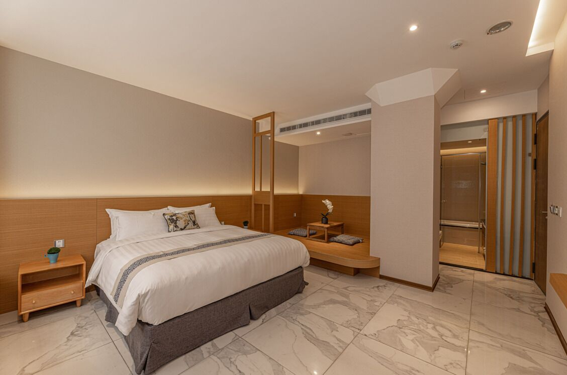 A modern hotel room with a large bed, a bedside table, a small table with a vase, and a mirror.