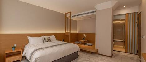 A modern hotel room with a large bed, a bedside table, a small table with a vase, and a mirror.