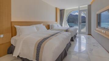 Habitación de hotel con dos camas, un ventanal con vistas a las montañas y un balcón con barandilla.
