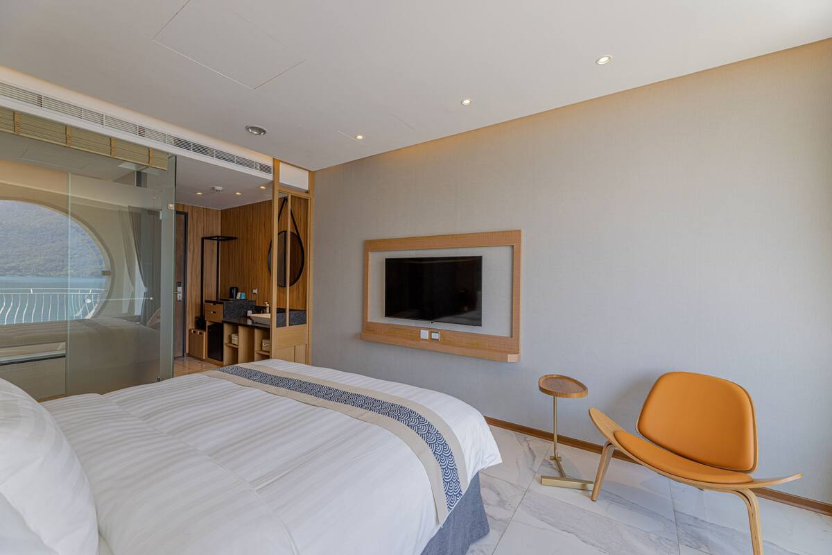 A modern hotel room with a large bed, a television mounted on the wall, and a seating area with a chair.
