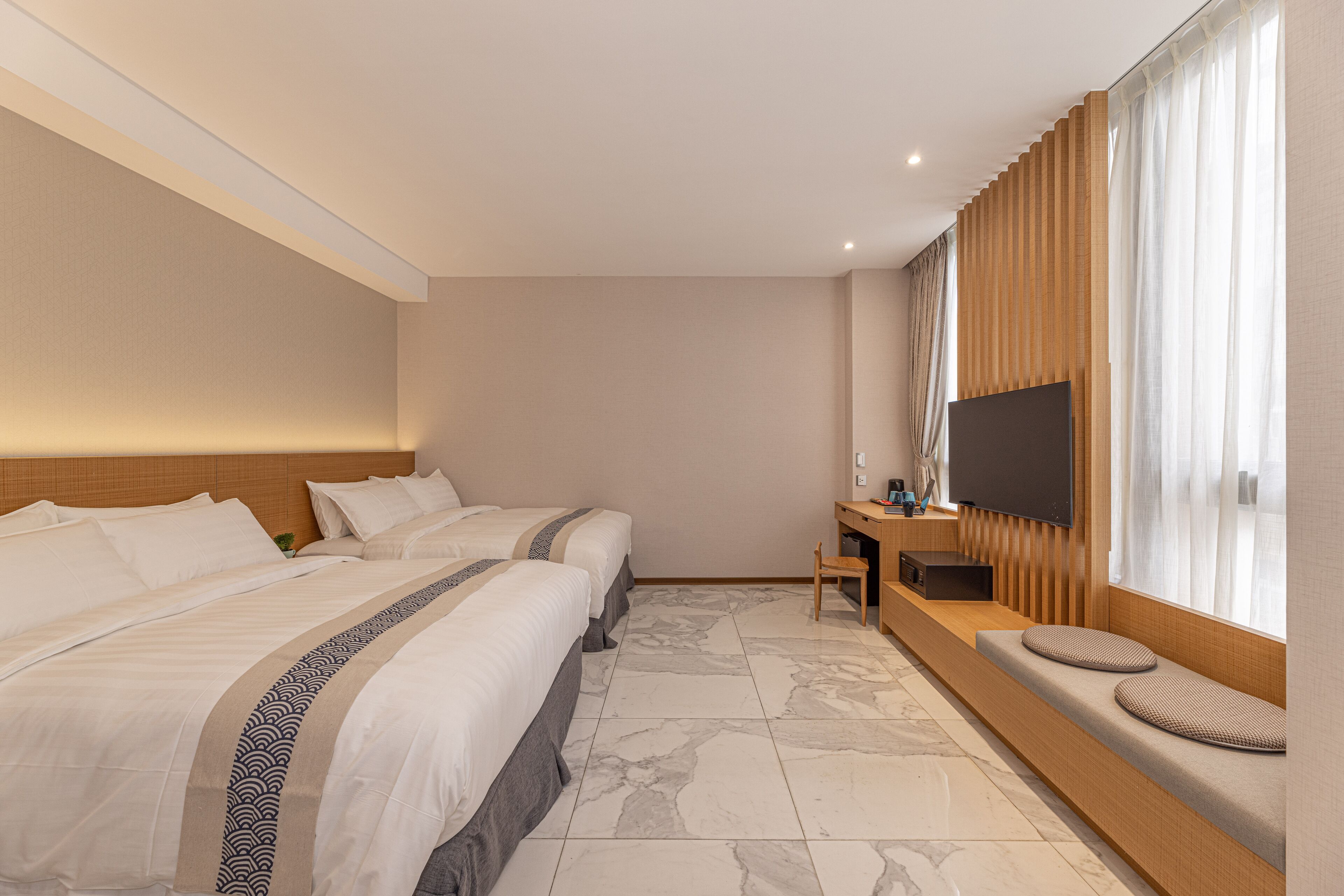 A hotel room with two beds, a TV, a desk, and a window with curtains.