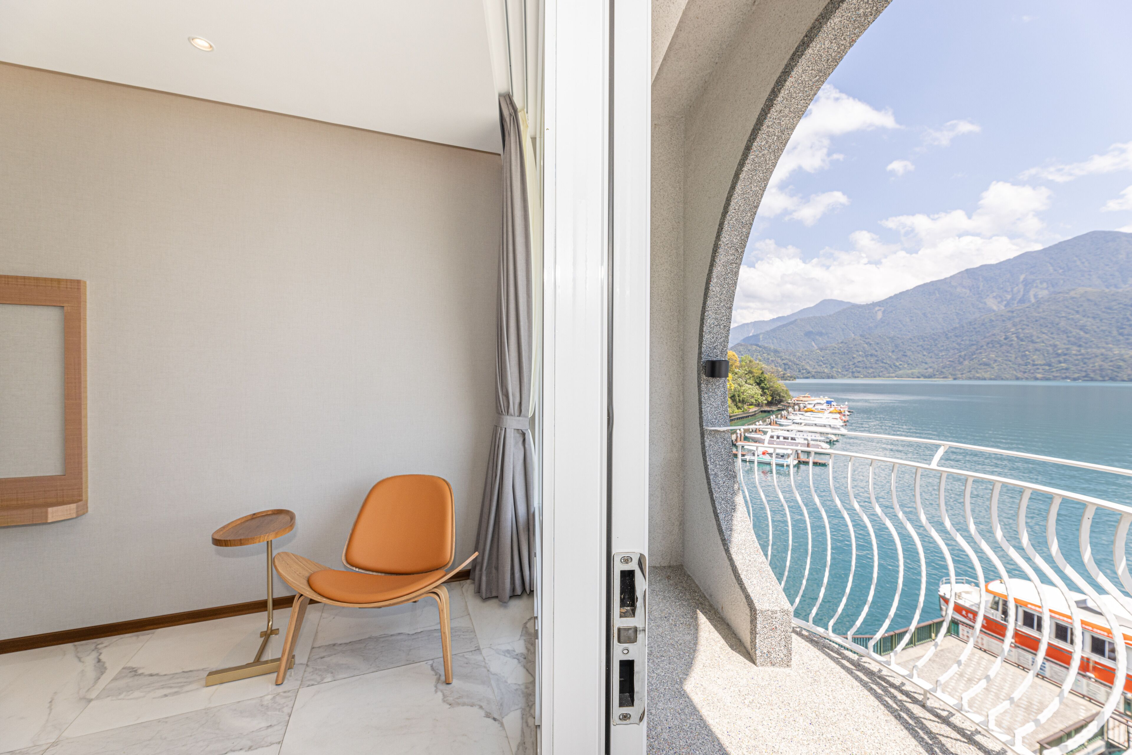 Un balcón con vista a un lago y botes, una silla y una mesita.