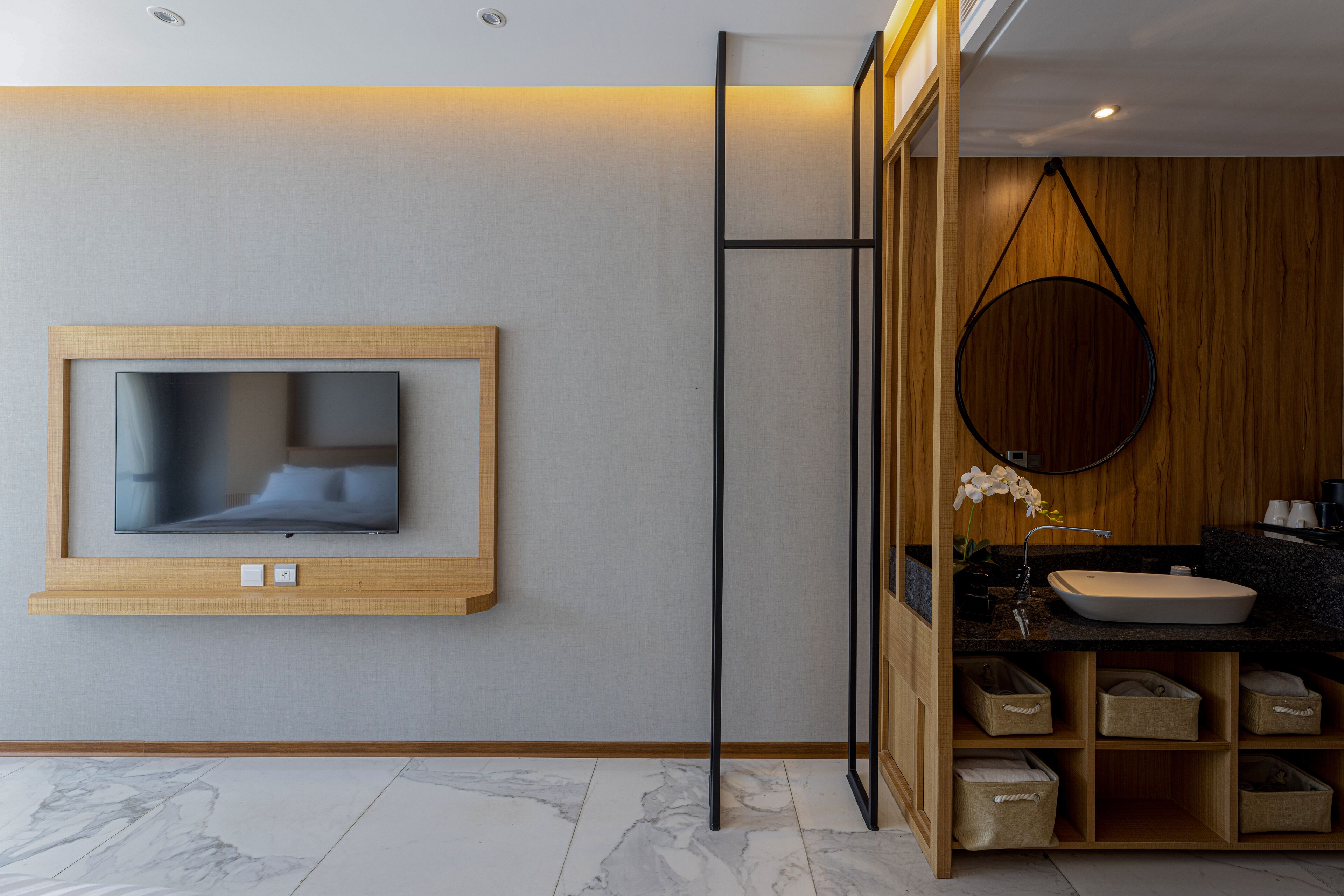 Un baño moderno con tocador de madera, un espejo redondo y televisor integrado.
