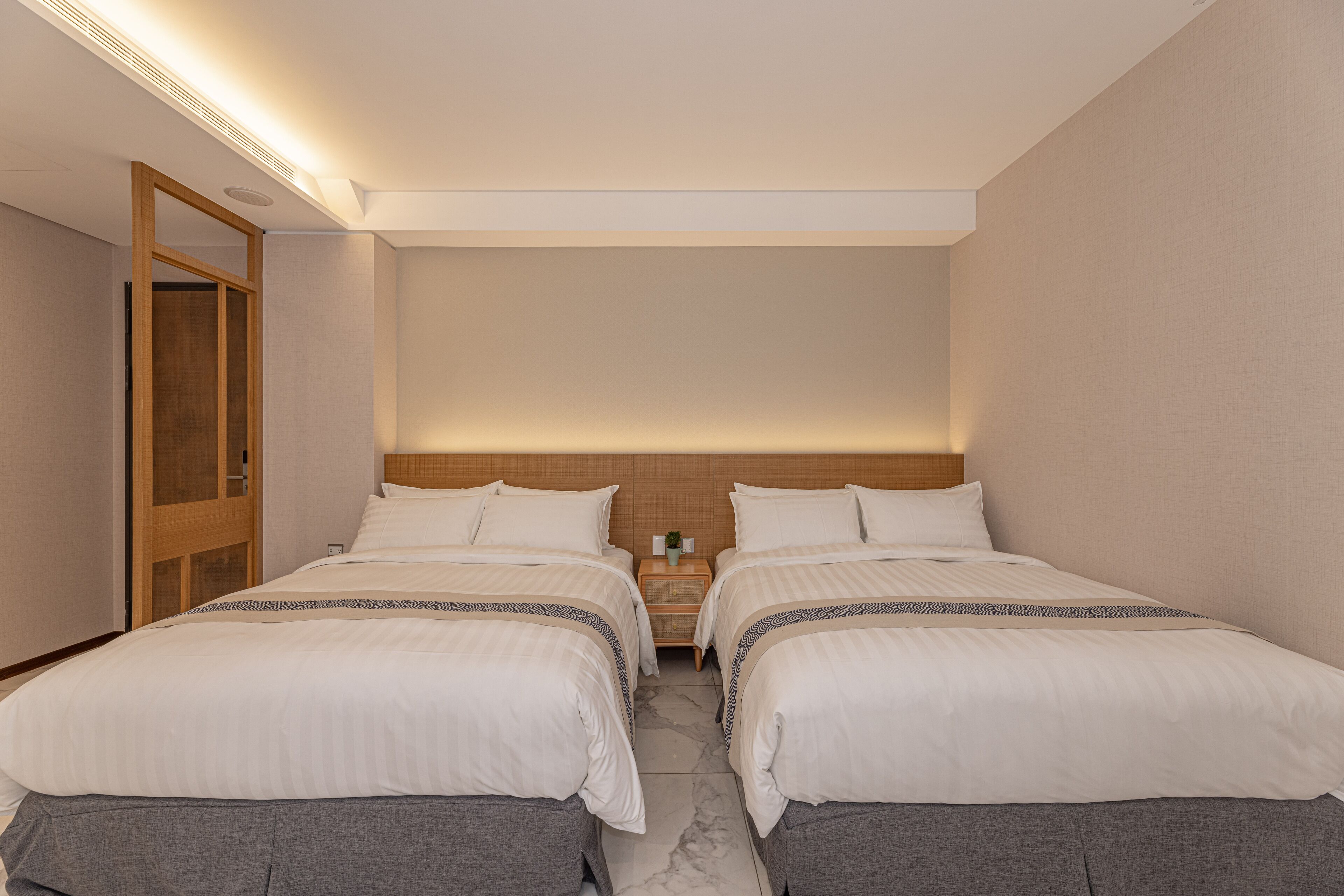 Una habitación de hotel con dos camas, cabecero de madera, mesita de noche con lámpara y espejo.
