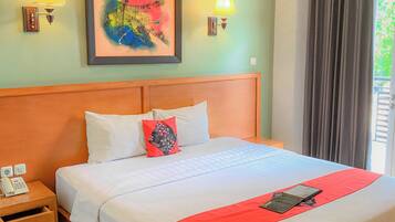 Habitación de hotel con una cama grande, una mesita de noche con teléfono, dos lámparas de pared, un cuadro colorido sobre la cama y una ventana con cortinas.