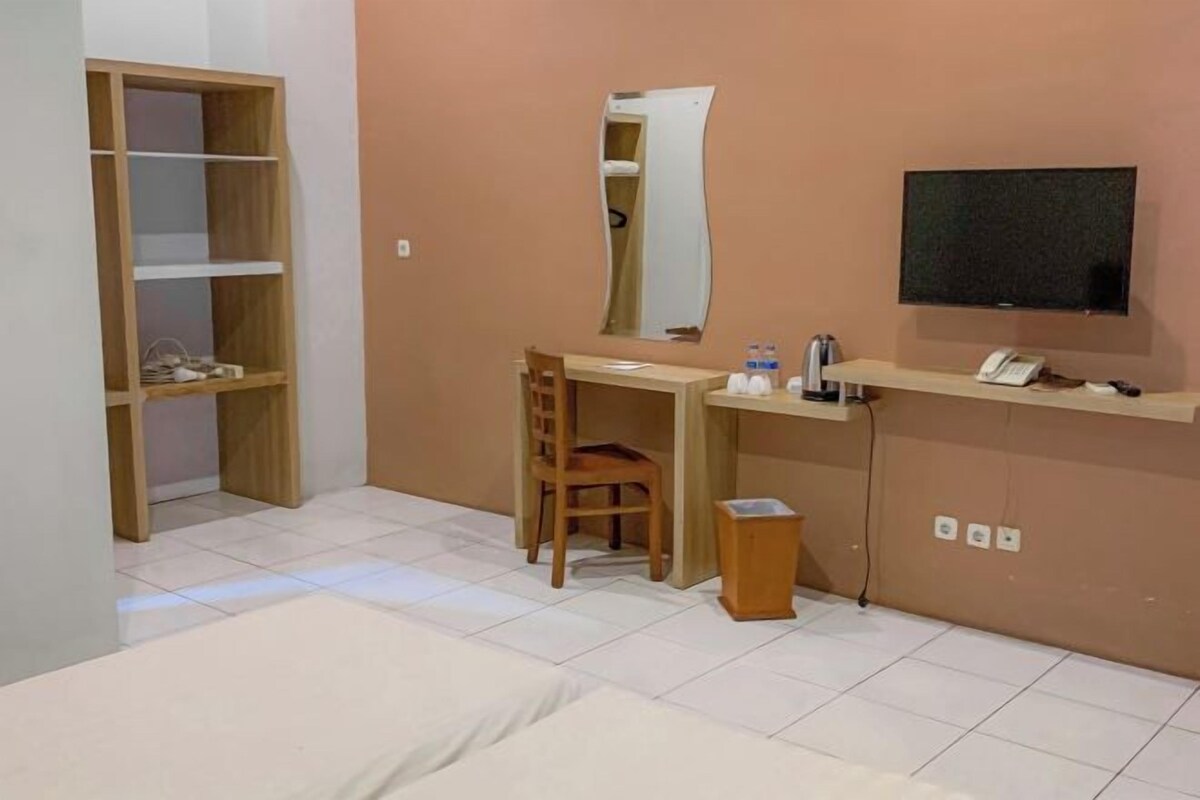A hotel room with a bed, a desk, a chair, a TV, a wardrobe, and a small trash bin.