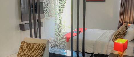A modern hotel room with a sofa, a coffee table, a bed with a red blanket, a painting on the wall, and a TV mounted on the wall.