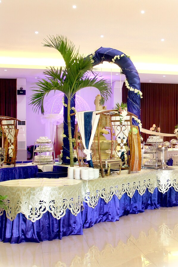 Un espacio para eventos decorado, con un escenario, arreglos florales y un soporte escalonado para pasteles.