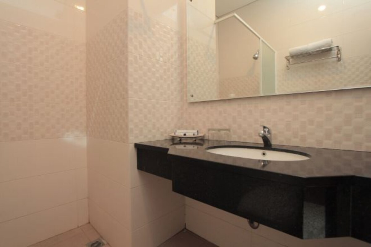Un baño con encimera negra, lavabo blanco y un espejo encima.