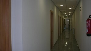 Un long couloir étroit, avec des portes en bois d’un côté et un extincteur fixé au mur de l’autre.