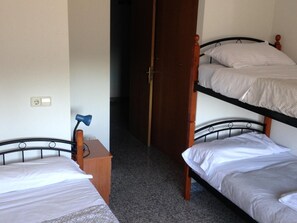 Een slaapzaal met stapelbedden, een bureau met lamp en een deur naar een andere kamer.