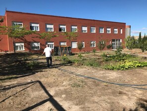 Een gebouw van rode baksteen met meerdere ramen en een tuin vol bomen en planten.