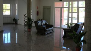 Un hall d’entrée spacieux avec un sol ciré, deux canapés en cuir, des plantes en pot et une grande porte-fenêtre coulissante donnant sur l’extérieur.