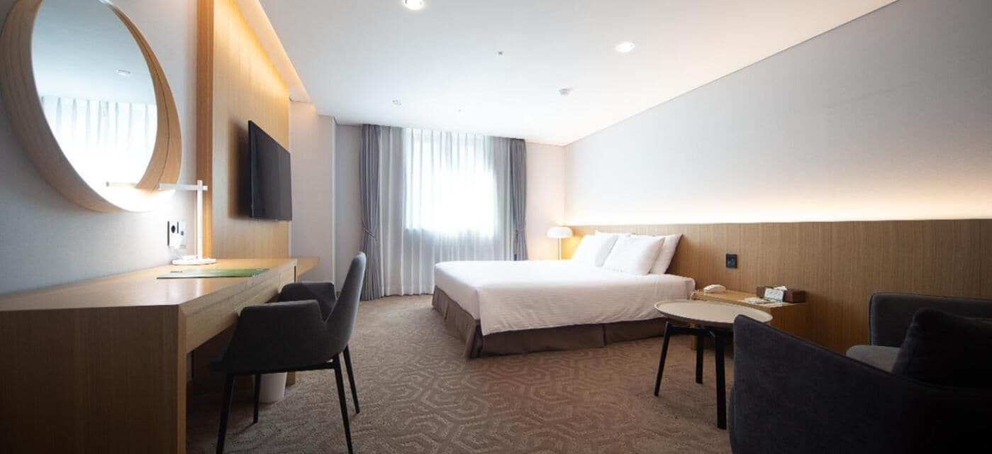 Habitación de hotel con cama, escritorio con silla, una mesa redonda y televisor montado en la pared.