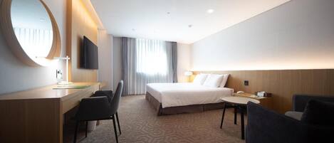 Habitación de hotel con cama, escritorio con silla, una mesa redonda y televisor montado en la pared.