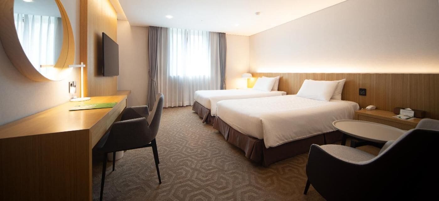 Habitación de hotel con dos camas, un escritorio con silla, televisor y una mesita.