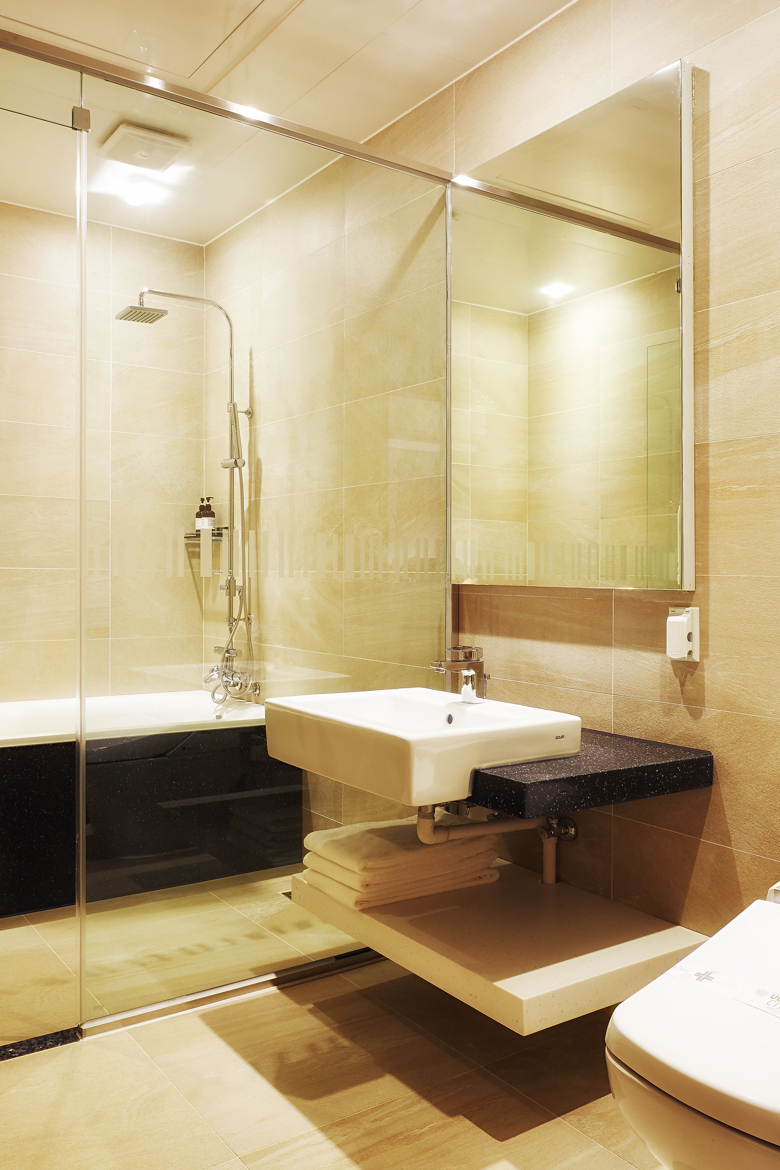 Ein modernes Badezimmer mit einer gläsernen Duschkabine, einem weißen Waschbecken und einem großen Spiegel.
